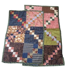 May include: Two patchwork quilts with a variety of patterned fabrics in shades of blue, pink, brown, and green. The quilts feature a mix of floral, striped, and geometric designs, with a green border.