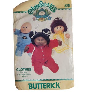 Puede incluir: Patrón de costura Butterick vintage para ropa de Cabbage Patch Kids. El patrón presenta ilustraciones de tres muñecas Cabbage Patch Kids con diferentes atuendos. El patrón está en un sobre color crema con el logotipo de Cabbage Patch Kids y el número 329.