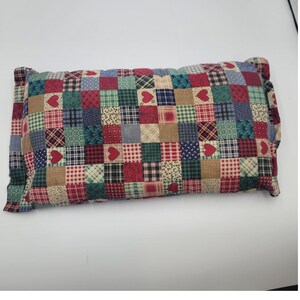 May include: A rectangular throw pillow featuring a patchwork design of small squares in various patterns, including red hearts, green and red plaid, blue and white dots, and tan textures. The fabric has a multi-colored, quilted appearance.