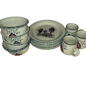 Puede incluir: Un juego de vajilla de cerámica que incluye cuencos, platos y tazas de color blanco roto con un borde azul moteado. Las piezas están decoradas con un gráfico en marrón y negro de casas para pájaros sobre una valla y finas ramas con hojas.