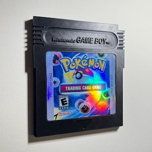 May include: Black Nintendo Game Boy cartridge featuring the Pokémon Trading Card Game. The cartridge has a colorful label with the Pokémon logo, a Poké Ball, and the text "TRADING CARD GAME". The ESRB rating is visible.