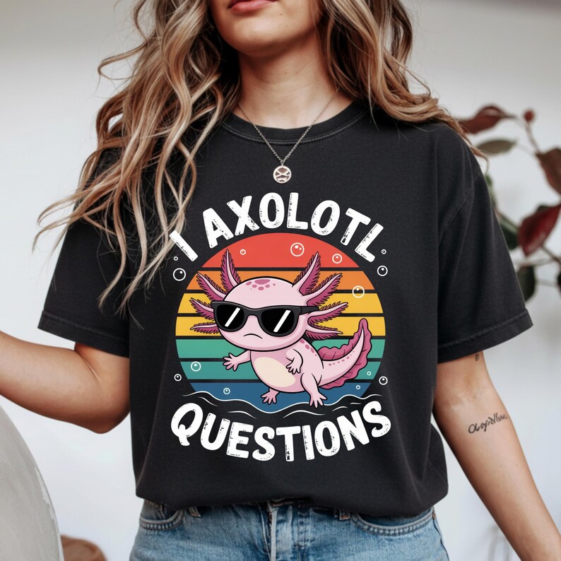 May include: Black t-shirt featuring a cartoon axolotl wearing sunglasses, set against a colorful sunset design. The text "I AXOLOTL QUESTIONS" is printed above and below the axolotl illustration. The shirt is a casual wear item.