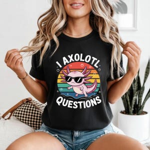 Könnte beinhalten: Schwarzes T-Shirt mit einem Cartoon-Axolotl, das eine Sonnenbrille trägt, vor einem farbenfrohen Sonnenuntergang. Der Text "I AXOLOTL QUESTIONS" ist darunter gedruckt. Ein lustiges Grafik-T-Shirt.