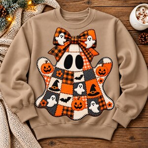 Peut inclure: Un sweat-shirt beige à manches longues orné d'un grand motif central représentant un fantôme composé de carrés en patchwork orange, noir et blanc. Le fantôme porte un grand nœud à carreaux orange et noir et est décoré de citrouilles et chauves-souris.
