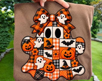 May include: A brown t-shirt featuring a large, central ghost-shaped appliqué. The ghost is composed of a patchwork of orange, black, and white plaid and gingham patterns, decorated with embroidered ghosts, jack-o'-lanterns, bats, and hats.
