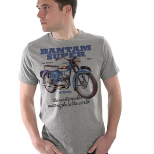 Pode incluir: Camiseta cinza com um desenho de motocicleta azul e branca. O texto na camiseta diz "BANTAM SUPER", "175cc", "Two Stroke" e "a motocicleta mais popular do mundo".