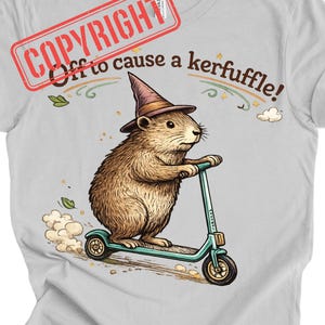 Könnte beinhalten: Hellgraues T-Shirt mit einem Cartoon-Murmeltier, das einen Hexenhut trägt und einen türkisfarbenen Roller fährt. Der Text "Off to cause a kerfuffle!" ist über dem Murmeltier aufgedruckt. Ein Copyright-Stempel ist oben links sichtbar.