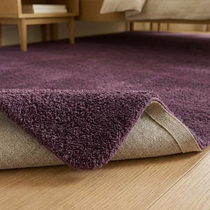 Ultra soft purple plush area rug styled in a modern minimalist living room with elegant neutral furniture and cozy natural lighting. This thick fluffy shag carpet features a luxurious high-pile texture that adds warmth, comfort, and sophistication to contemporary interiors. Perfect for bedrooms, apartments, nurseries, dorm rooms, and aesthetic home decor setups. The rich deep violet color creates a bold yet calming statement piece that blends beautifully with Scandinavian, modern, boho.
