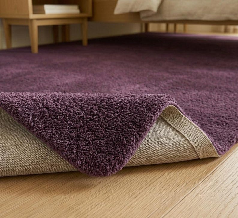 Ultra soft purple plush area rug styled in a modern minimalist living room with elegant neutral furniture and cozy natural lighting. This thick fluffy shag carpet features a luxurious high-pile texture that adds warmth, comfort, and sophistication to contemporary interiors. Perfect for bedrooms, apartments, nurseries, dorm rooms, and aesthetic home decor setups. The rich deep violet color creates a bold yet calming statement piece that blends beautifully with Scandinavian, modern, boho.