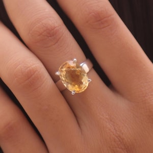 Könnte beinhalten: Ein Silberring mit einem großen, oval geschliffenen, durchscheinenden gelben Citrin-Edelstein, der von vier Krappen gehalten wird. Die Ringschiene ist aus glattem, poliertem Silber. Der Text LuxurySilver925 ist auf der Fassung sichtbar.
