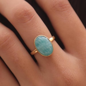 Peut inclure: Une bague en or avec une pierre précieuse ovale bleu clair. Le corps de la bague est en or poli. La pierre a une surface lisse et est sertie dans une lunette en or. Un bijou.