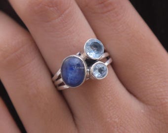 Könnte beinhalten: Ein Silberring mit einem großen, ovalen, tiefblauen Stein und zwei kleineren, runden, hellblauen Steinen in Zargenfassung. Die Ringschiene besteht aus drei dünnen Silberdrähten, die in einen Schaft übergehen. Der Text Luxury Silver ist sichtbar.