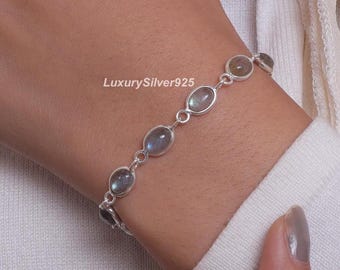 May include: A silver bracelet featuring oval-shaped, iridescent gemstones. The gemstones are linked together with small silver connectors. The bracelet is worn on a wrist, and the text "LuxurySilver925" is visible.