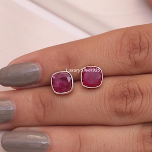 Könnte beinhalten: Ein Paar quadratisch geschliffene Rubin-Ohrstecker mit Silberfassung. Die Ohrringe haben eine leuchtend rote Farbe und werden auf hellem Hintergrund präsentiert. Der Text "Luxury Silver925" ist sichtbar.