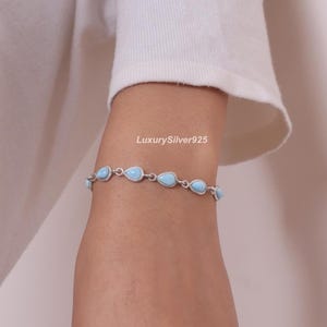 May include: A silver chain bracelet featuring a series of light blue, teardrop-shaped stones set in metal frames. The bracelet is displayed on a wrist, with the text LuxurySilver925 visible above the jewellery piece, which consists of multiple links.
