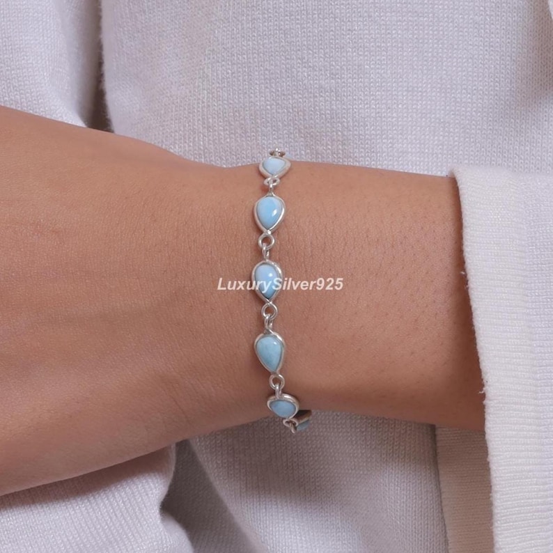 May include: A silver chain bracelet featuring five teardrop-shaped light blue stones set in metal frames. The bracelet is linked together with small silver rings. The text LuxurySilver925 is visible in the centre of the image near the stones.