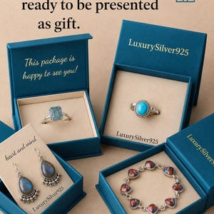 May include: Four teal jewellery boxes containing silver jewellery. One box holds a rectangular blue stone ring, another a round turquoise ring, one a pair of teardrop labradorite earrings, and the last a bracelet with multi-coloured stone links.