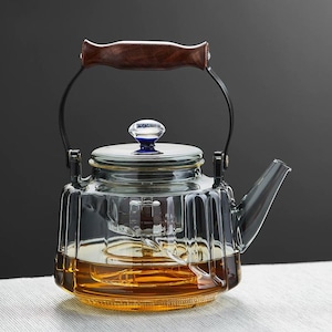 May include: A clear glass teapot with a wooden handle and a blue knob on the lid. The teapot has a ribbed design and contains a golden-brown liquid, likely tea. The handle is attached to the pot with black metal supports.