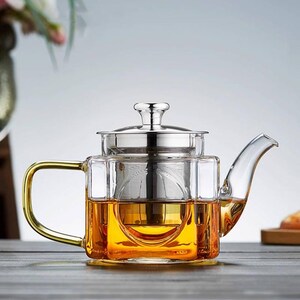 May include: A clear glass teapot with a gold handle and a stainless steel infuser. The teapot is filled with amber-colored tea. The design is modern and elegant, suitable for brewing loose leaf tea.