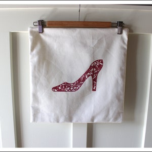 May include: A white canvas tote bag with a red glitter design of a high-heeled shoe.