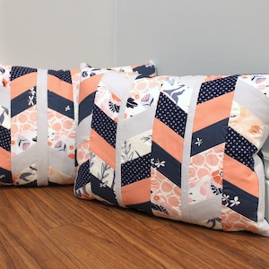May include: Two decorative throw pillows with a chevron pattern in shades of peach, gray, white, and navy blue.