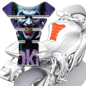 May include: A motorcycle with a custom tank protector featuring a detailed image of the Joker's face. The protector is multi-layered and includes the word "JOKE" in a graffiti style. An orange tank pad is also visible.