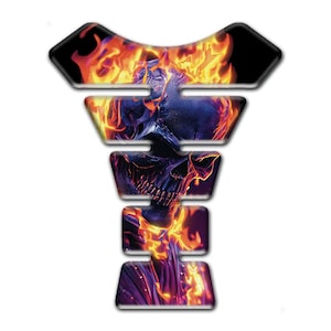 May include: A motorcycle tank pad with a fiery skull design. The pad is black with a detailed image of a skull engulfed in flames, featuring shades of orange, red, and blue. The shape is designed to fit the contours of a motorcycle tank.