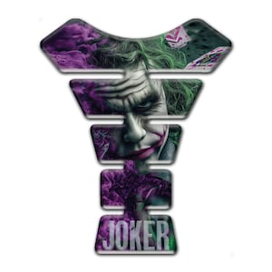 Peut inclure: Un protège-réservoir de moto avec une image détaillée du Joker. Le design comprend le visage du Joker, ses cheveux verts et des effets de fumée violets, avec le mot "JOKER" en bas. Le coussinet a une forme multicouche.