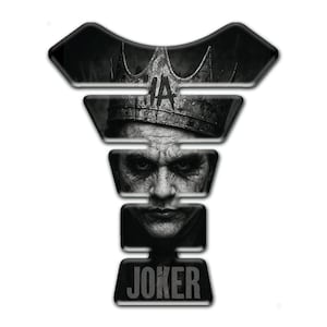 May include: Black and white motorcycle tank protector featuring a detailed image of the Joker wearing a crown. The word "JOKER" is printed in bold, white letters at the bottom of the protector. The design is a stylized portrait.