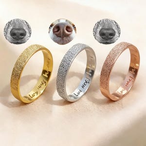Könnte beinhalten: Drei Ringe in Gold, Silber und Roségold, jeweils mit strukturierter Oberfläche und eingraviertem Text. Die Ringe werden mit Bildern von Hundenasen präsentiert. Der goldene Ring sagt "Lucy lucky", der silberne Ring sagt "Lucy lucky" und der roségoldene Ring sagt "in my heart".