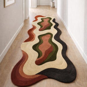 Pode incluir: Tapete abstrato com design ondulado. Apresenta uma paleta de cores quentes, incluindo tons de castanho, bege, verde e preto. Colocado sobre um ch&atilde;o de madeira num corredor, adiciona um toque moderno ao espa&ccedil;o.