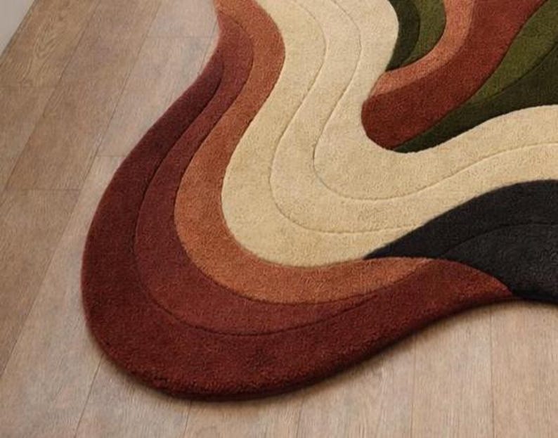 Pode incluir: Um tapete abstrato com um design ondulado e org&acirc;nico. O tapete apresenta uma paleta de cores que vai do vermelho profundo ao laranja, passando pelo bege, verde-oliva e preto, criando um efeito texturizado e sobreposto. Est&aacute; colocado sobre um ch&atilde;o de madeira clara.