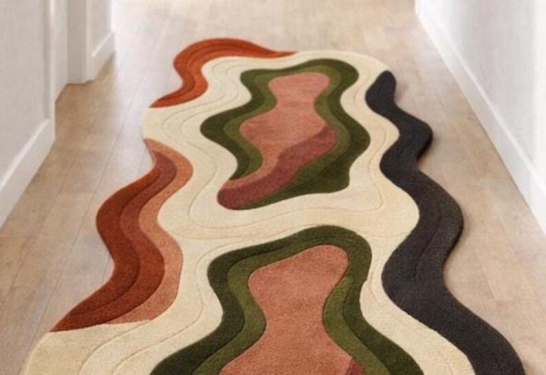 Pode incluir: Um tapete abstrato com um design ondulado e em camadas. A paleta de cores do tapete inclui ferrugem, creme, verde-oliva e cinza carv&atilde;o. &Eacute; colocado sobre um piso de madeira clara, adicionando um toque moderno ao espa&ccedil;o. Medidas em cent&iacute;metros.