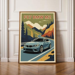 Puede incluir: Una impresión artística enmarcada que presenta un coche deportivo BMW M2 azul claro conduciendo por una carretera sinuosa a través de un paisaje montañoso. La obra de arte tiene un estilo vintage de cartel de viaje con el texto "F87 BMW M2" en la parte superior.
