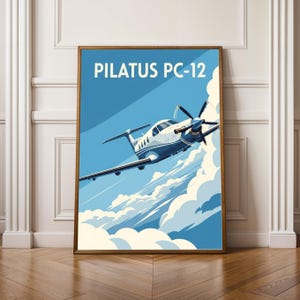 May include: A framed art print depicting a Pilatus PC-12 aircraft in flight against a blue sky with white clouds. The print has the text "PILATUS PC-12" at the top. The aircraft is white and blue, with a retro style.