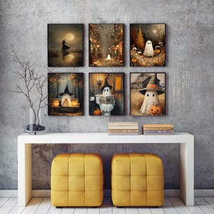 May include: A collection of six framed Halloween-themed art prints. Each print features a whimsical ghost character in various spooky settings, including a witch, a moonlit scene, and a pumpkin. The artwork is displayed above a white console table with two yellow cube ottomans.
