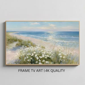 May include: A framed landscape painting of a beach scene. The artwork depicts a sandy beach, ocean waves, and a blue sky with clouds. White flowers and green grass are in the foreground. The text "FRAME TV ART | 4K QUALITY" is at the bottom.