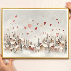 May include: A framed watercolor print featuring a winter village scene with snow-covered houses and evergreen trees. Red and pink hearts float in the sky above the village. The frame is gold.