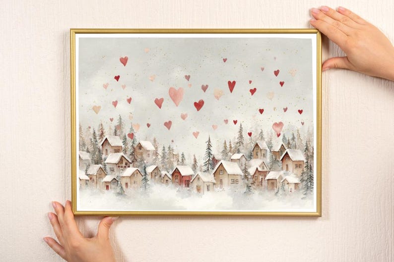 May include: A framed watercolor print featuring a winter village scene with snow-covered houses and evergreen trees. Red and pink hearts float in the sky above the village. The frame is gold.