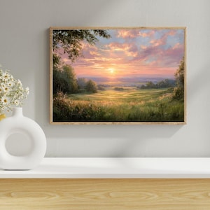 Peut inclure: Peinture de paysage encadrée représentant un lever de soleil sur un champ herbeux. Le ciel est rempli de nuages roses et oranges, et le soleil est un orbe jaune vif. Le tableau est dans un cadre en bois et est exposé sur une surface blanche.