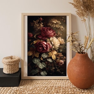 May include: A framed floral print featuring a bouquet of red roses and cream-colored flowers against a dark background. The artwork includes green leaves and yellowed foliage, creating a vintage aesthetic. The frame is light-colored wood.