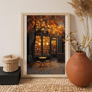 May include: Framed print of a cozy bookstore exterior at dusk. The shop features a glass front with visible bookshelves, a small table and chairs, and a tree with autumn leaves and string lights. The scene is warm and inviting, with a vintage aesthetic.