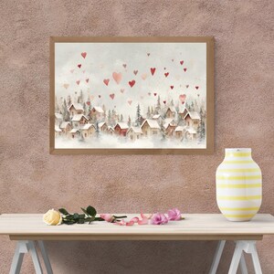 May include: Watercolor painting of a winter village scene with red hearts floating in the sky. The artwork features small houses nestled among evergreen trees, framed in a light brown wooden frame. A yellow and white striped vase sits on a wooden table.