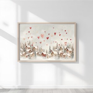 May include: Watercolor painting of a village nestled among evergreen trees, with red heart shapes floating in the sky. The artwork is framed in a light wood frame, creating a cozy and romantic scene.