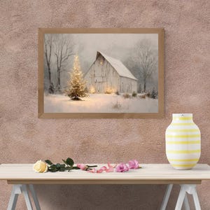Puede incluir: Una pintura enmarcada de un paisaje invernal representa un granero cubierto de nieve y un árbol de Navidad iluminado. La obra de arte está en un marco de madera y está colocada contra una pared texturizada de color marrón rosado. Un jarrón a rayas amarillas y blancas y flores están sobre una mesa al frente.