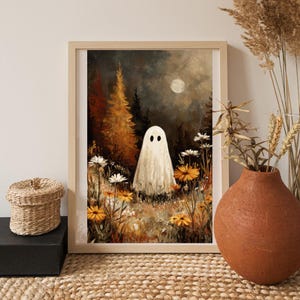 May include: A framed art print featuring a whimsical ghost in a field of wildflowers under a moonlit sky. The artwork has a vintage aesthetic with warm tones of orange, brown, and cream. The ghost has two black eyes.