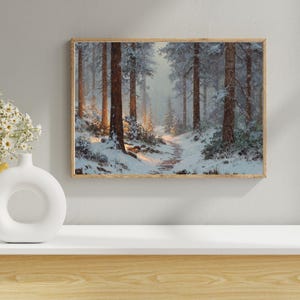 Könnte beinhalten: Ein gerahmtes Landschaftsgemälde zeigt eine verschneite Waldszene. Hohe, braune Baumstämme erheben sich aus dem schneebedeckten Boden, mit einem Pfad, der sich durch die Bäume schlängelt. Das Kunstwerk befindet sich in einem Holzrahmen, und die Farbpalette ist gedämpft mit Weiß-, Braun- und Grautönen.