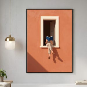 May include: A framed wall art print featuring an illustration of a person sitting in a window frame reading a blue book. The wall is a solid terracotta orange color with a white window frame. The person wears light-colored pants and brown shoes.