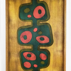 Pode incluir: Uma peça de arte abstrata enquadrada com um design verde e vermelho. A obra de arte é feita de madeira e apresenta uma série de círculos e ovais sobrepostos.