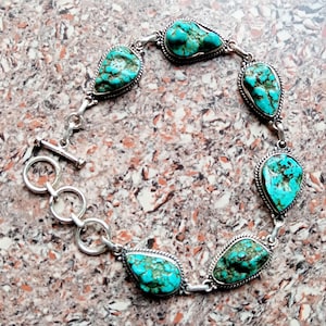 May include: A silver bracelet with seven turquoise gemstones. The teardrop-shaped stones are set in silver bezels and linked together. The bracelet fastens with a toggle clasp.
